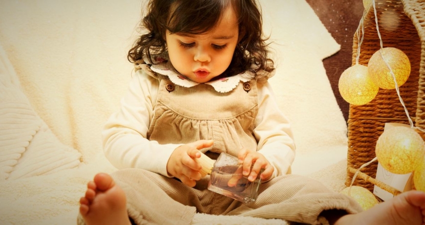 Petite fille découvrant le parfum Premier Sourire de Chamboule Tout, près d'une maison en osier et de guirlandes lumineuses de Noël